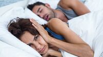 Woman blocking ears with hands while man snoring on bed
