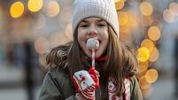 Little girl enjoying a lollipop on a winter city street with warm lights