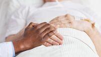 Close up of caring African-American doctor holding hands with senior patient lying in hospital bed, copy space