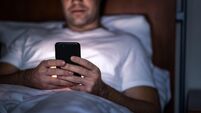 Phone in bed at night. Man with smartphone before sleeping. Secret texting, cheating or working late. Happy guy browsing online