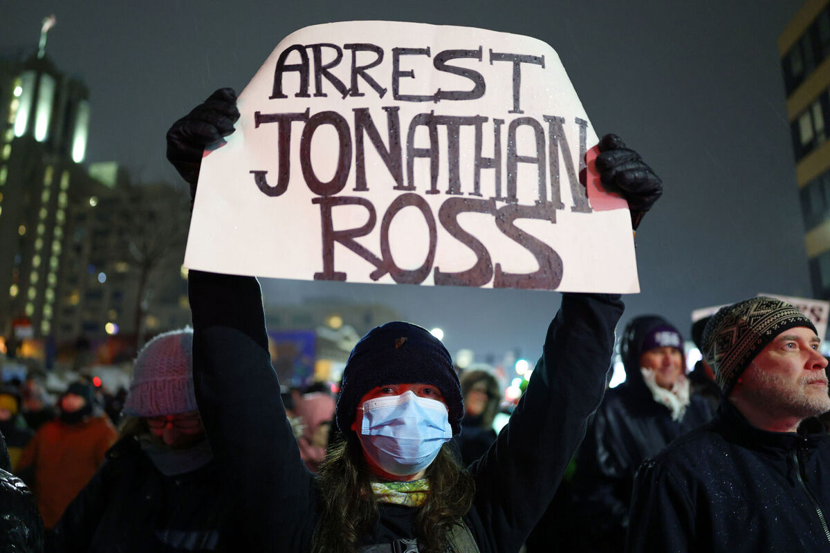 A protester holds a sign reading "ARREST JONATHAN ROSS" during a rally for Renee Good after she was fatally shot. Picture: Adam Bettcher/AP