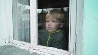 A lonely orphan boy looks through an old window.