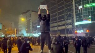 <p>In this frame grab from video obtained by the AP outside Iran, a masked demonstrator holds a picture of Iran's Crown Prince Reza Pahlavi during a protest in Tehran, Iran. (UGC via AP)</p>