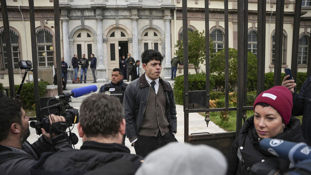 <p>Seán Binder (centre) is one of 24 people charged with people smuggling, belonging to a criminal organisation and money laundering — three extremely serious felony charges that could result in 20-year prison sentences for the defendants. File photo: AP/Panagiotis Balaskas</p>