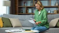 Serious and confused senior woman in glasses sitting on sofa at home. Worriedly holding the phone and documents in his hands. Pr