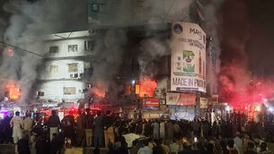 People gather as firefighters try to control the fire (Mohammad Farooq/AP)