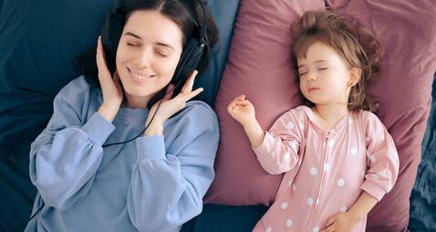 Mother Wearing Headphones Listening a Podcast While Baby Sleeps