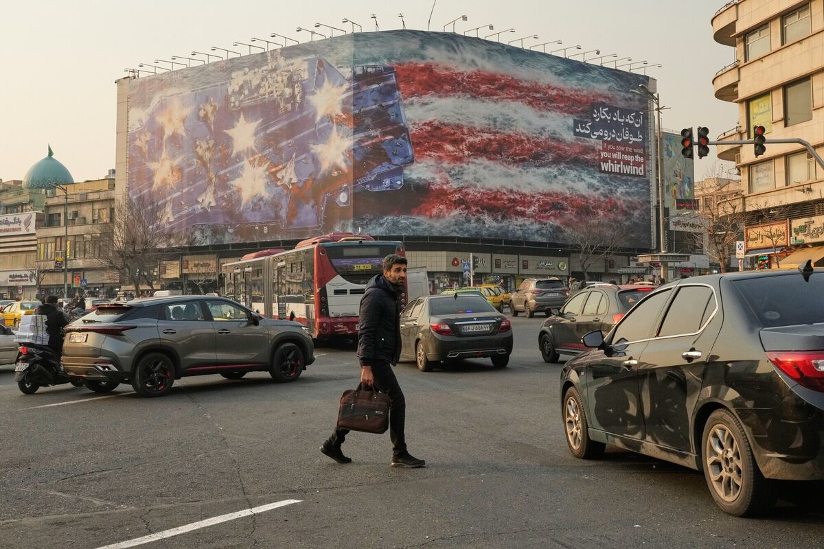A man walks among vehicles in front of a billboard depicting a damaged U.S. aircraft carrier with disabled fighter jets on its deck and a sign reading in Farsi and English, "If you sow the wind, you'll reap the whirlwind," at Enqelab-e-Eslami (Islamic Revolution) Square in Tehran, Iran. Picture: AP Photo/Vahid Salemi