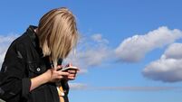 Teen girl playing online games by a smartphone on blue sky background. The concept of teenage addiction to a mobile phone and so
