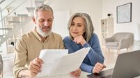 Middle aged couple reading paper bills calculating pension using laptop at home.
