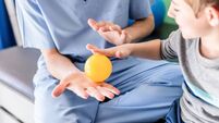 Unrecognizable occupational therapist with little male patient doing a hand exercise with a small ball