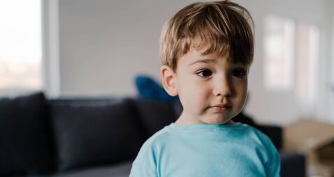 Portrait of a little boy in blue at home standing in the middle of the room