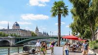 People strolling and biking on the banks of the Seine between palm trees, picnic tables and parasols during Paris-Plages event,