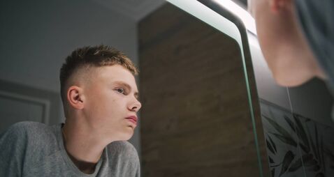 Teenager stands near wash basin and touches his face