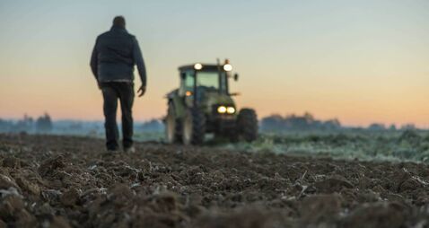 Male farmer with short brown hair,walking in the direction to his tractor,standing next to his agricultural field in the evening