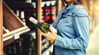 Customer buying white wine or sparkling drink. Alcohol aisle in store or supermarket. Woman holding bottle. Buying riesling or c