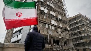 <p>A man holds an Iranian flag as he looks at the damaged façade of Gandhi Hospital in Tehran. Picture: AP Photo/Vahid Salemi</p>