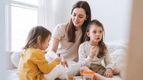 Young happy family with one parent woman mother with two children girls eating cookies on bed room at home