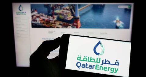 Person holding cellphone with logo of Qatari petroleum company QatarEnergy on screen in front of business webpage. Focus on phon