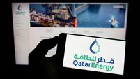 Person holding cellphone with logo of Qatari petroleum company QatarEnergy on screen in front of business webpage. Focus on phon
