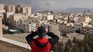 <p>A man looks through biculars as a plume of smoke rises after a military strike on the capital Tehran. Picture: ATTA KENARE / AFP via Getty Images</p> <p>A man looks through biculars as a plume of smoke rises after a military strike on the capital Tehran. Picture: ATTA KENARE / AFP via Getty Images</p>