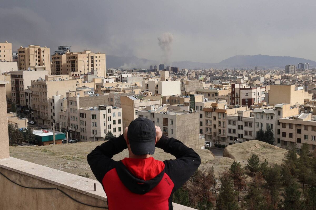 A man looks through binoculars as a plume of smoke rises after a military strike on the capital Tehran. Picture:  ATTA KENARE / AFP via Getty Images
