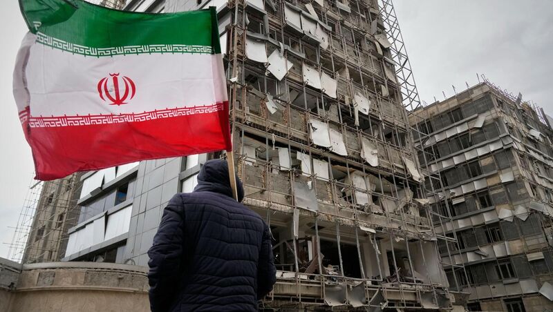 A man holds an Iranian flag as he looks at the damaged façade of Gandhi Hospital. Pic: Vahid Salemi/AP