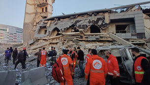 <p>Rescue workers gather in front of the destroyed centre of a Lebanese Islamic group hit by an Israeli strike, in the southern port city of Sidon, Lebanon (Mohammed Zaatari/AP)</p>