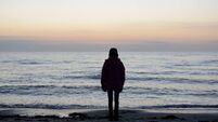 Rear View Of Silhouette Girl Standing At Beach Against Sky During Sunset