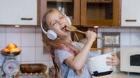 Little girl enjoying music while preparing food in kitchen