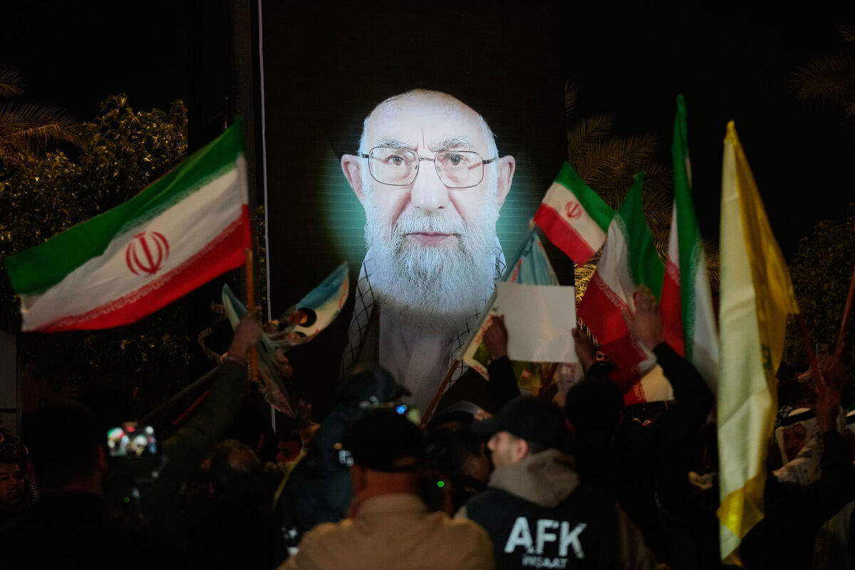 Protesters wave Iranian flags as another holds up an image of Supreme Leader Ayatollah Ali Khamenei, who was killed by a U.S. airstrike in Tehran, during a symbolic funeral in Baghdad, Iraq, Friday, March 6, 2026. (AP Photo/Hadi Mizban)