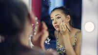 Teenage girl is applying make-up in her room